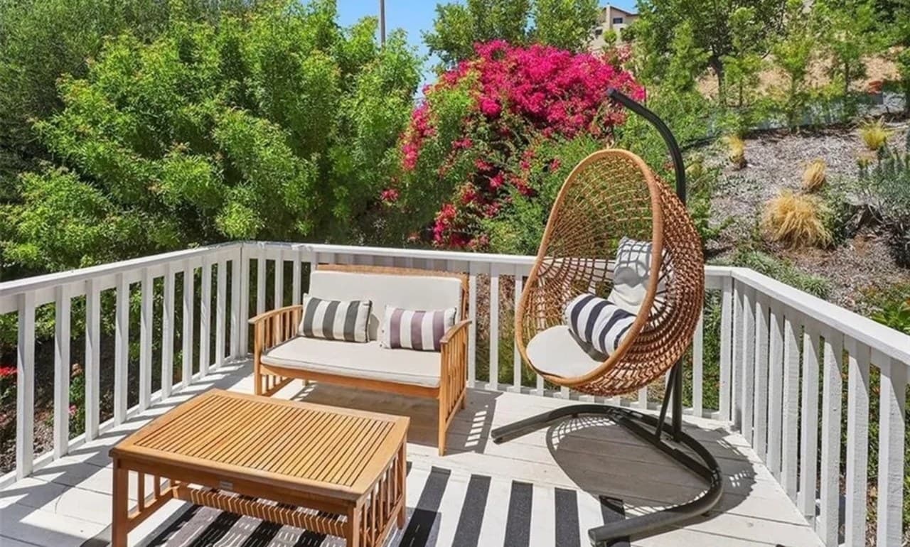An outdoor deck with a hanging chair, bench seating and bougainvillea in bloom behind the railing.