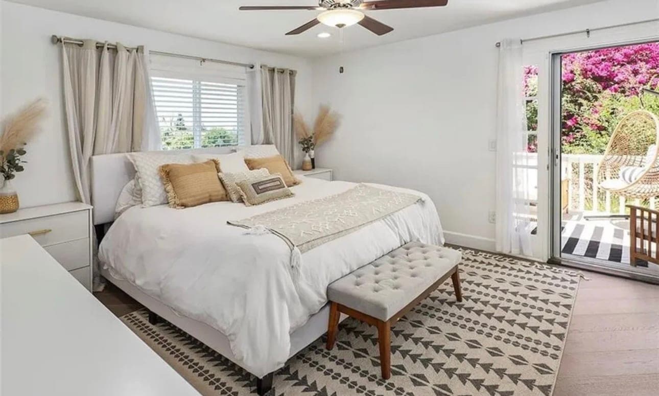 A bedroom with a made bed, a bench at its foot and doors out to a deck.
