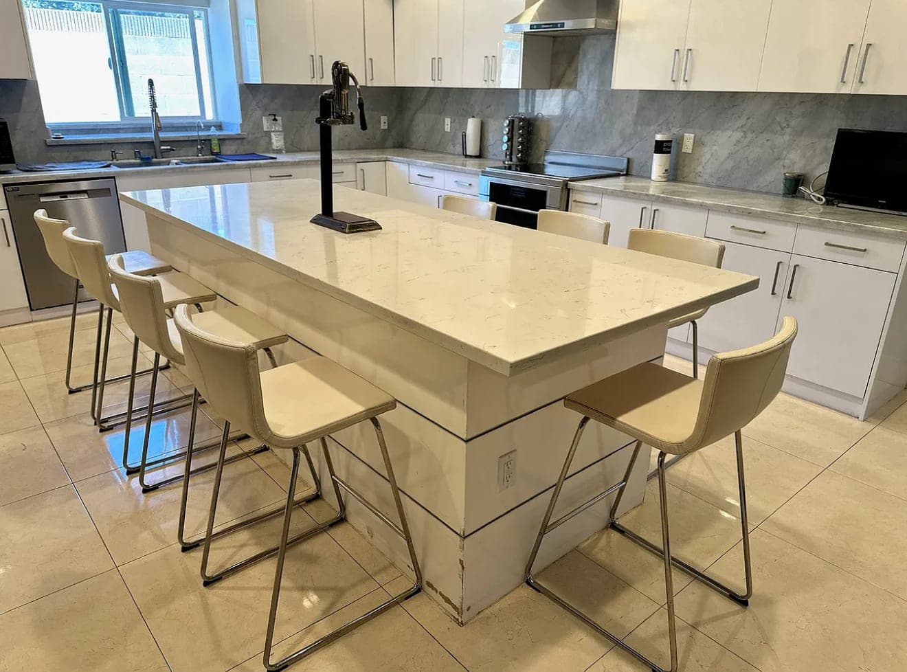 A kitchen island in white stone, with bar stools along one side.