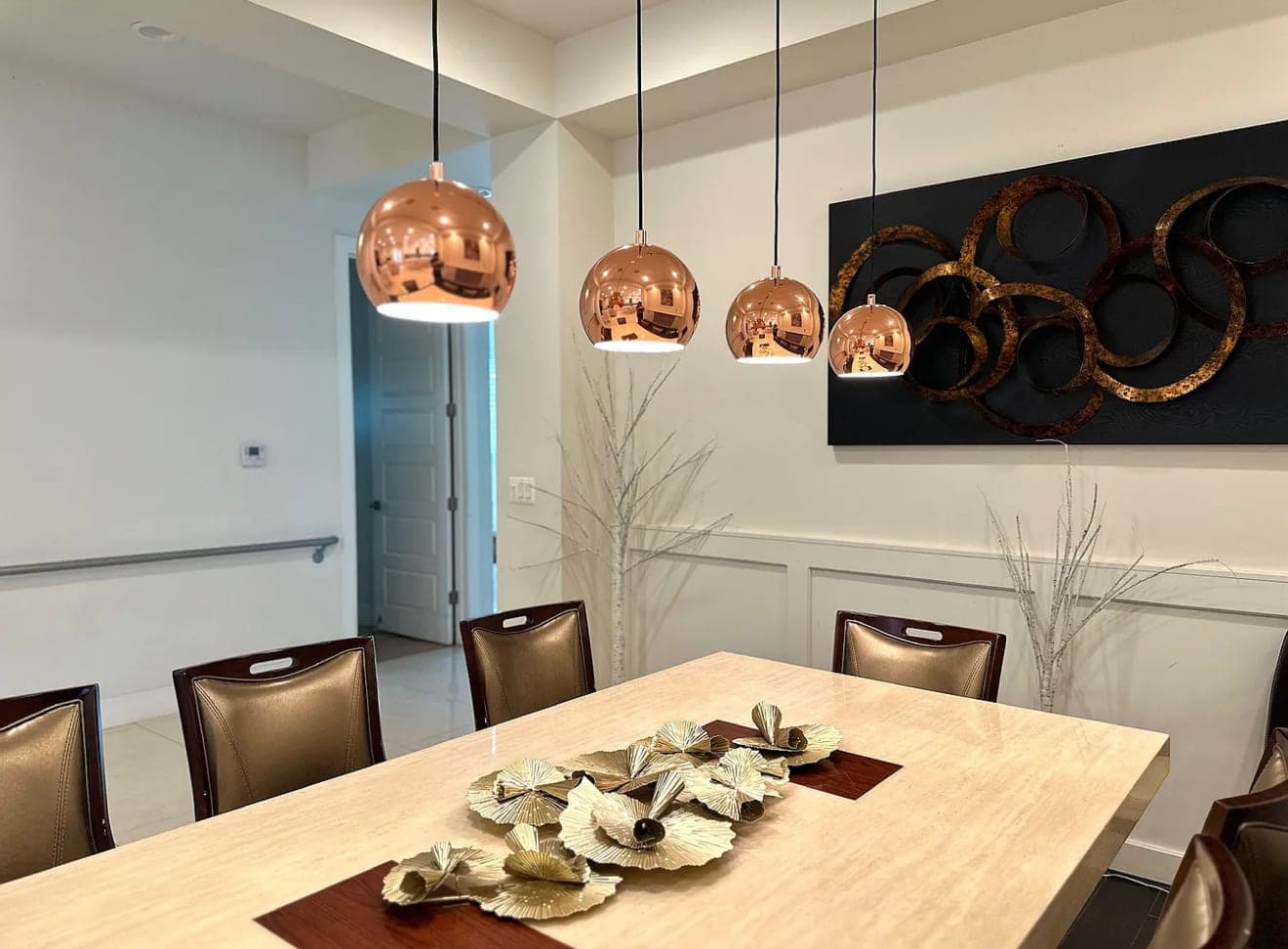 A dining table laid for a meal under three copper pendant lights.