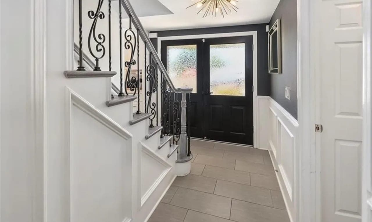 An entrance hall with a wrought-iron stair rail and a dark front door.