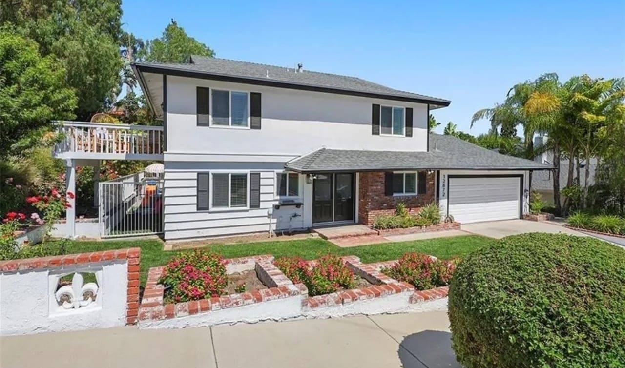 A two-storey house behind a lawn, with brick planters and a paved driveway.