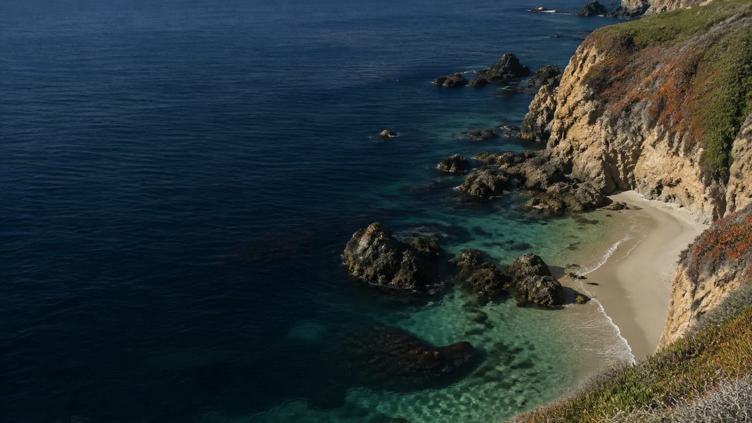 A Southern California cove with sandstone cliffs, rock outcrops and clear water over sand.
