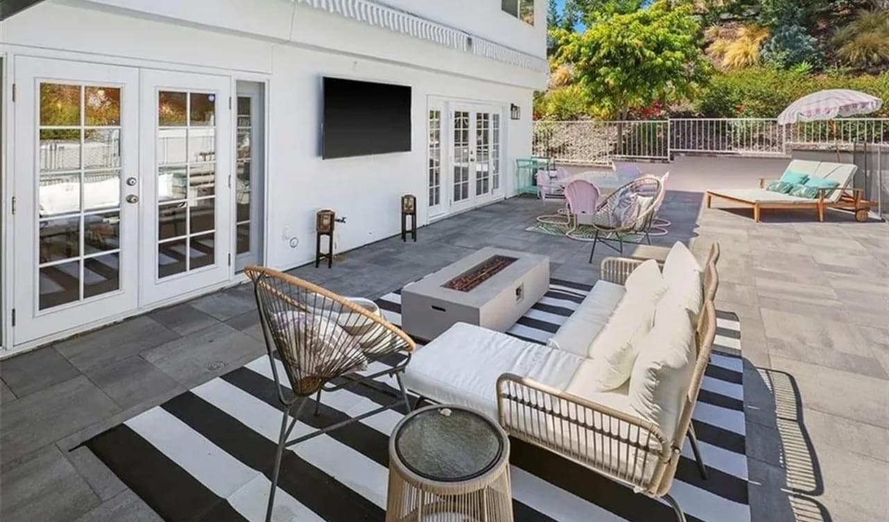 An outdoor patio with lounge chairs, a fire table and a planted hillside behind the railing.