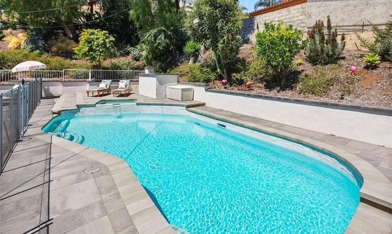 A backyard pool with a paved deck, a low wall and planting on the slope behind it.