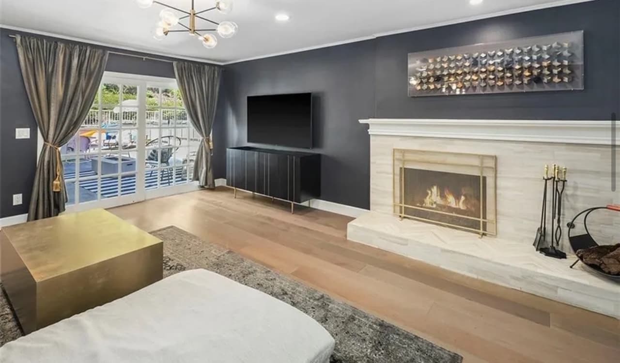 A living room with a fireplace and a dark accent wall, wood floors, and a large sectional sofa facing the hearth.