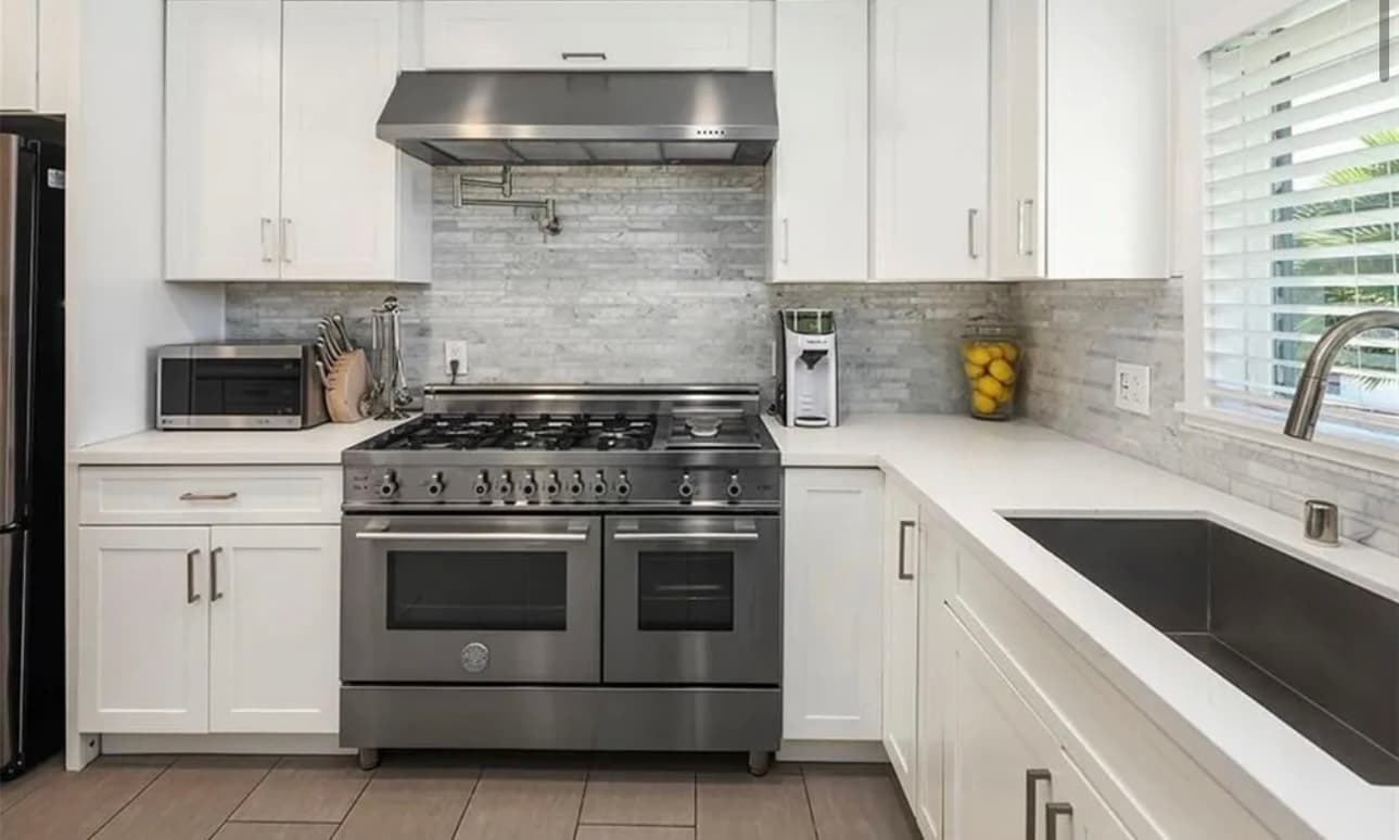 A white kitchen with a large range, a grey tile backsplash and a window over the sink.